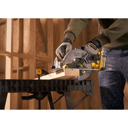 Photo of STANLEY SFMCS500M1S circular saw cutting wood on workbench in construction setting.