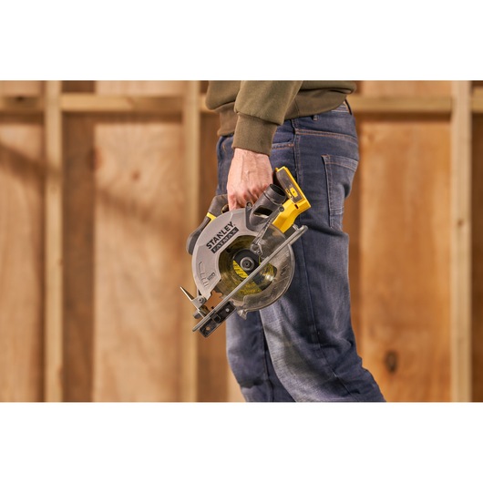 STANLEY SFMCS500M2K circular saw held by person in jeans, shown in a workshop setting.