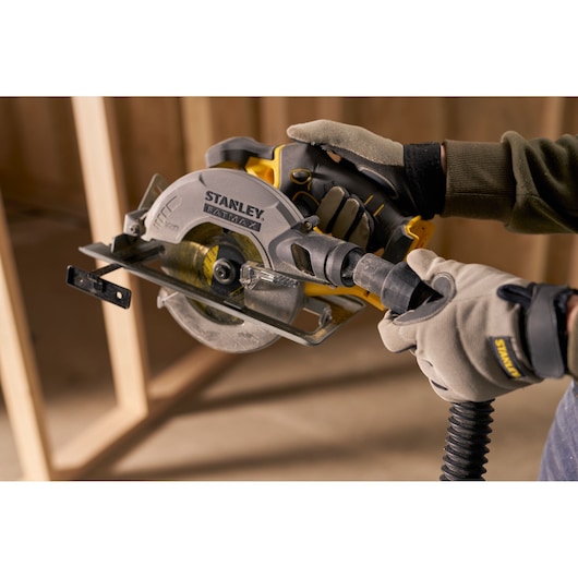 Photo of STANLEY SFMCS500M2K circular saw with vacuum hose attachment, held by gloved hands during construction.