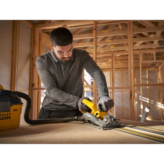Photo of STANLEY SFMCS551M1T circular saw in use, cutting wood with attached vacuum in a construction setting.
