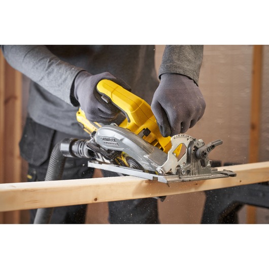 Photo of STANLEY SFMCS551M1T circular saw in use, cutting wood, handheld with gloves in workshop setting.