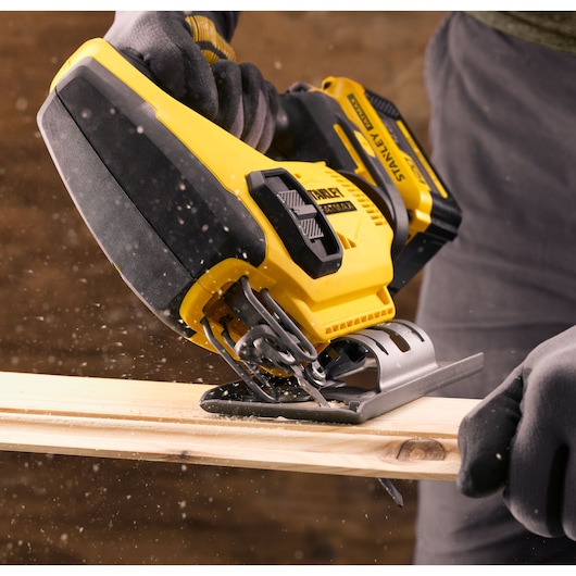 STANLEY SFMCS600B jigsaw cutting wood, close-up view, yellow and black power tool in use.