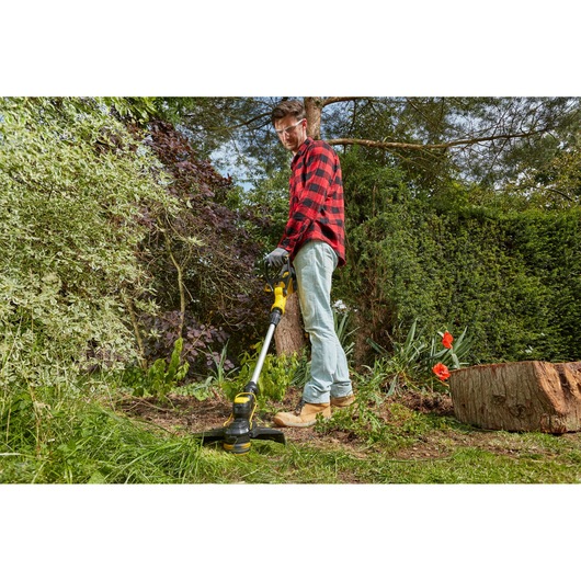 STANLEY SFMCST933B grass trimmer used in a garden, side view, with yellow and black design.