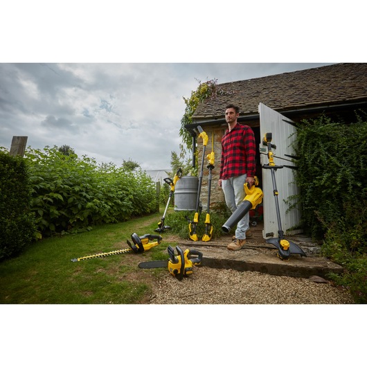 STANLEY SFMCST933B garden power tools in use outdoors near cottage, including trimmer, blower, hedge trimmer.
