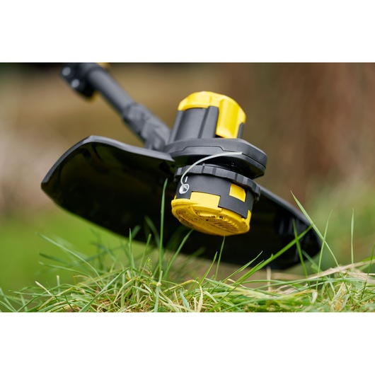 STANLEY SFMCSTB933B cordless string trimmer head close-up in grass, showing yellow and black design.