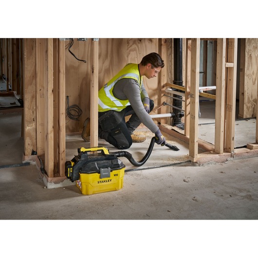 Person using a STANLEY V20 vacuum cleaner to clean construction dust inside a wooden framed building.