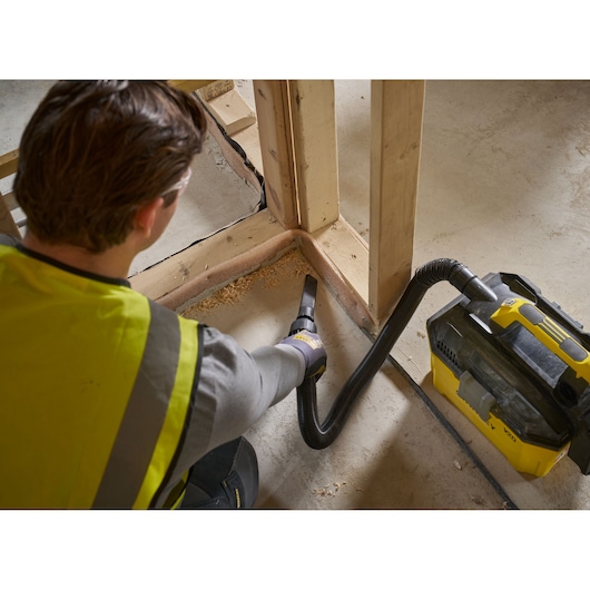Person cleaning construction site corner with a STANLEY SFMCV003L vacuum cleaner.