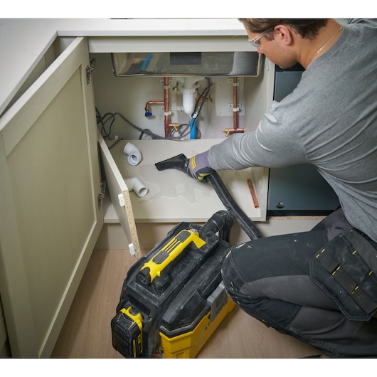 Person uses STANLEY wet/dry vacuum to clean water under sink in cabinet. Plumbing tools visible.