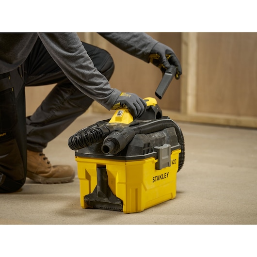 Person using a yellow STANLEY cordless wet/dry vacuum cleaner on a workshop floor.