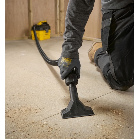 Person using a STANLEY vacuum cleaner to clean dust and debris from a workshop floor.