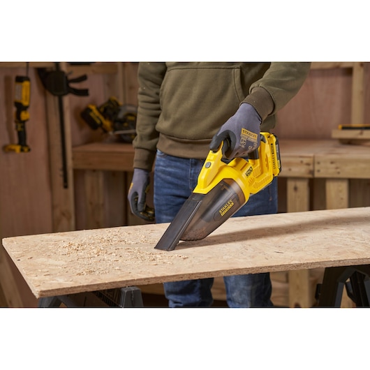 STANLEY SFMCVH001B handheld vacuum in use on wood surface, yellow body, clear dust container.