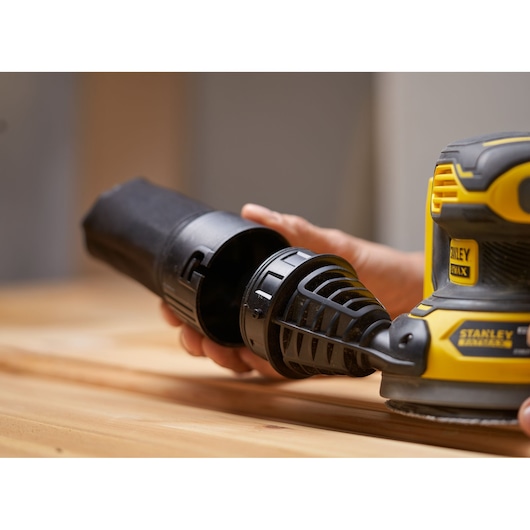 Photo of STANLEY SFMCW220D1S cordless random orbital sander in use, focusing on dust container removal.
