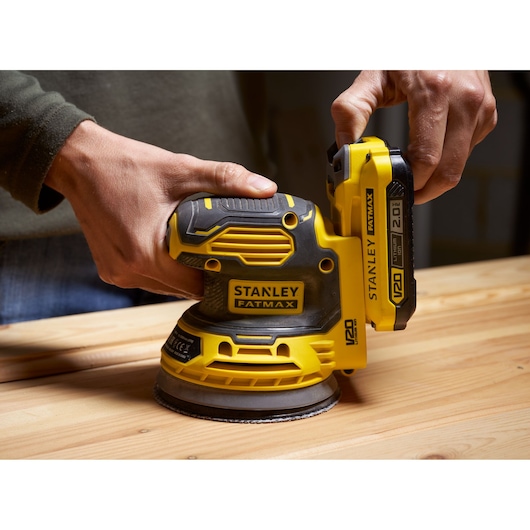 STANLEY SFMCW220D1S cordless sander, yellow and black, in use on wooden surface, close-up photo.