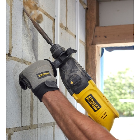 Stanley SFMEH200K hammer drill being used on a masonry wall, close-up view.