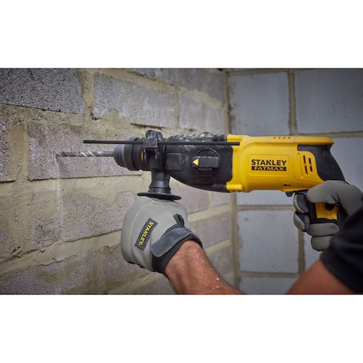 Photo of STANLEY SFMEH210K-QS rotary hammer drill being used on a brick wall, yellow and black design.