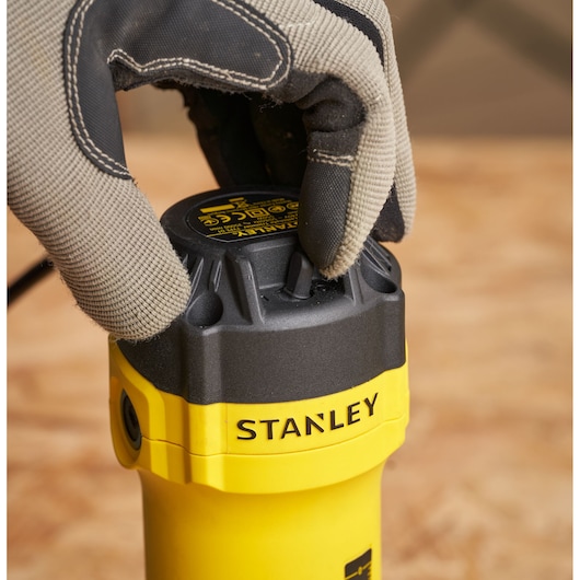 Photo of STANLEY ST55 power tool close-up, gloved hand adjusting black top knob, yellow tool body visible.