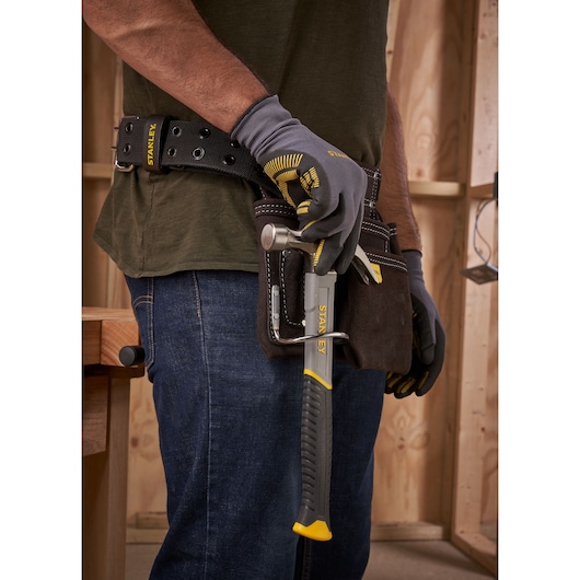 Photo of STANLEY STHT0-51309 hammer in tool belt, worker wearing gloves and jeans in workshop.