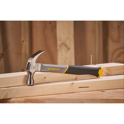 STANLEY STHT0-51309 claw hammer with black and yellow handle on wooden planks, side view.