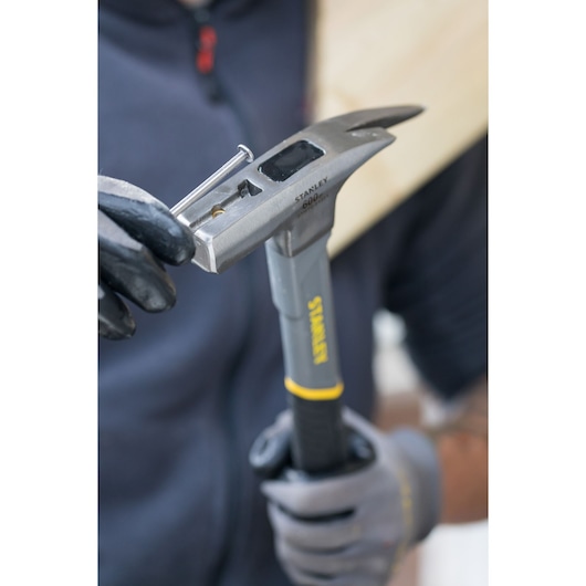 STANLEY STHT0-51311 hammer held in gloved hands, showing nail starter feature in use.
