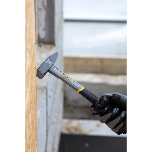 Stanley STHT0-51907 hammer with black and yellow handle used against wooden surface, photography close-up.