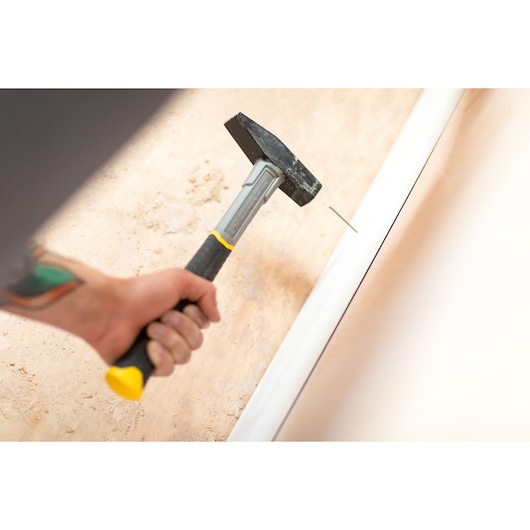 Photo of STANLEY STHT0-51908 hammer with yellow-black handle nailing trim against a wall.
