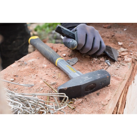 STANLEY STHT0-51909 sledge hammer with black handle on a workbench near metal fasteners and gloved hand.