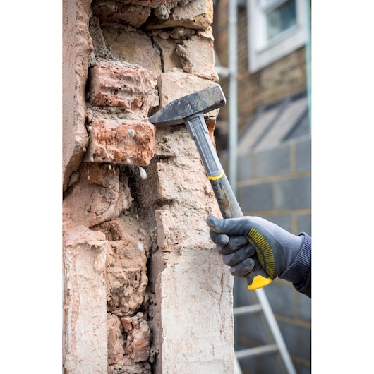 STANLEY STHT0-51909 demolition hammer used on a damaged brick wall, close-up with gloved hand.