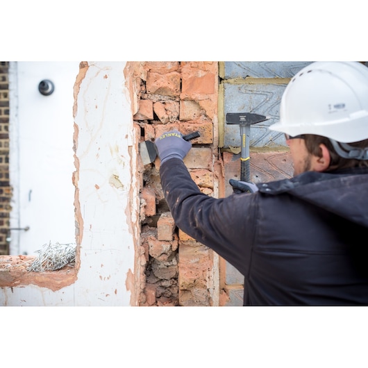 STANLEY STHT0-51910 chisel used on brick wall by worker wearing gloves and helmet.