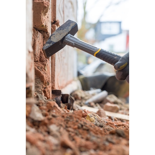 STANLEY STHT0-51910 club hammer with black and yellow handle shown breaking bricks during masonry work.