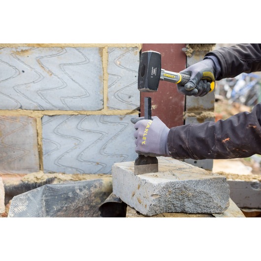 Photo of STANLEY STHT0-54128 sledge hammer in use, striking a chisel on a concrete block at a construction site.