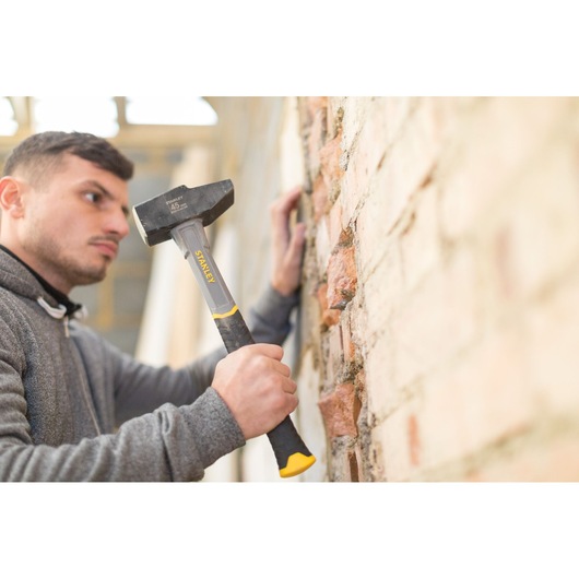 Stanley STHT0-54156 club hammer with black and yellow handle used on brick wall, angled side view.