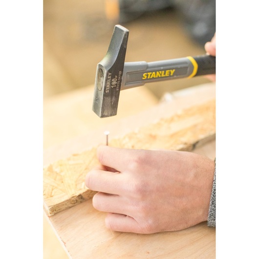 STANLEY STHT0-54158 claw hammer in use driving a nail into wood, close-up photography.