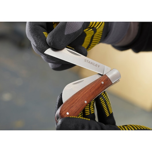 STANLEY STHT0-62687 folding pocket knife with wood handle, close-up held by gloved hands.