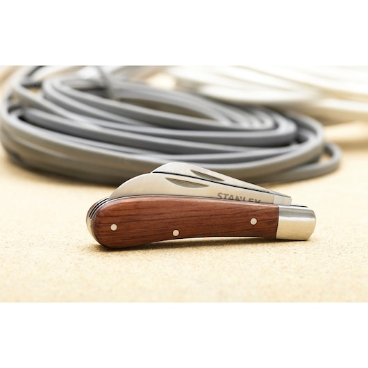STANLEY STHT0-62687 pocket knife with wood handle and folded blade on beige surface, coiled cables in background.