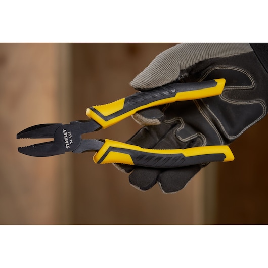 STANLEY STHT0-74367 combination pliers with yellow and black grip held in gloved hand, side angle.