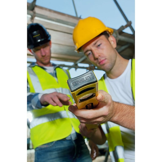 STANLEY STHT1-43102 spirit level held by workers in safety vests and helmets at construction site.