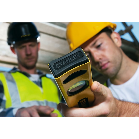 Photo of STANLEY STHT1-43102 level tool in use at construction site, close-up on yellow and black tool.