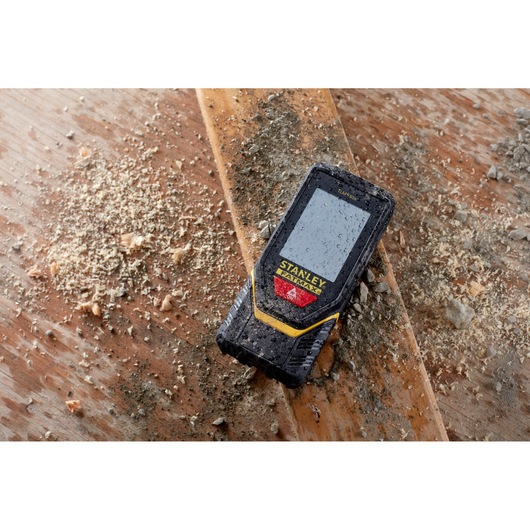 STANLEY STHT1-77139 laser distance measurer on dusty wood surface, rugged design, construction context.