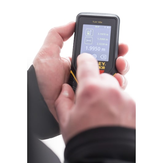 Photo of hands using STANLEY STHT1-77139 laser distance measurer, close-up on digital screen.