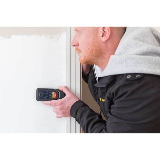 STANLEY STHT1-77142 digital laser measurer held in hand measuring distance on white wall.