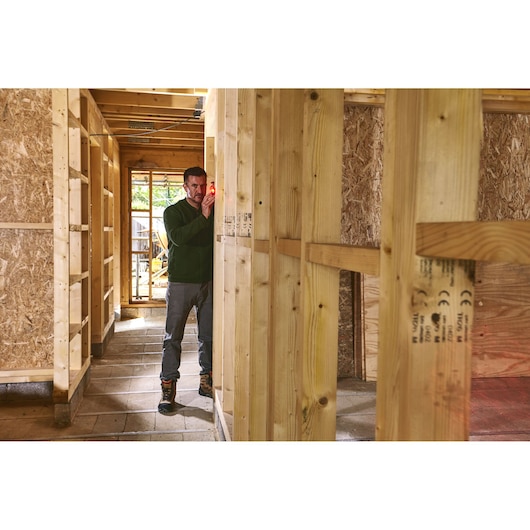 STANLEY STHT1-77409 laser measuring tool in use on construction site, person aligns tool to wooden frame.