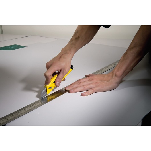 STANLEY STHT10265-0 utility knife cutting along a metal ruler on white surface, side angle photo.