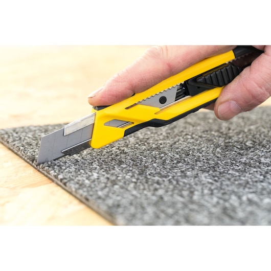 STANLEY STHT10266-1 utility knife cutting gray carpet, side view, yellow and black handle.