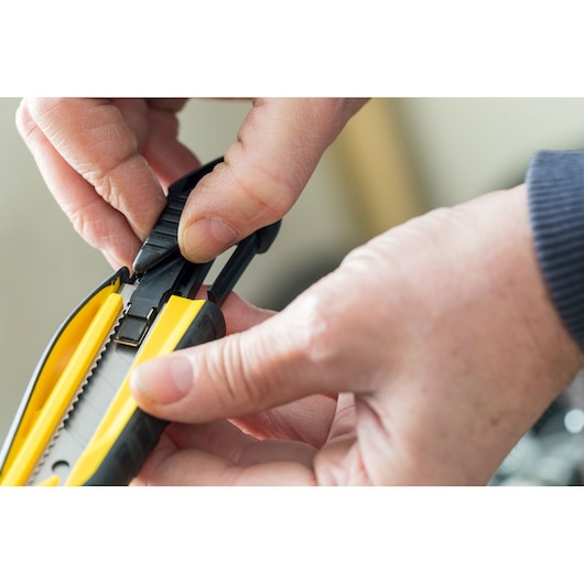 STANLEY STHT10270-0 utility knife close-up, yellow and black, hands adjusting blade slider.