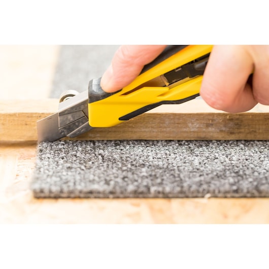 STANLEY STHT10270-0 utility knife cutting grey carpet next to wood, close-up photography.
