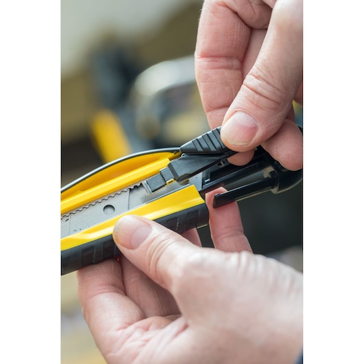 Close-up of hands adjusting STANLEY STHT10270-0 utility knife with yellow and black handle.