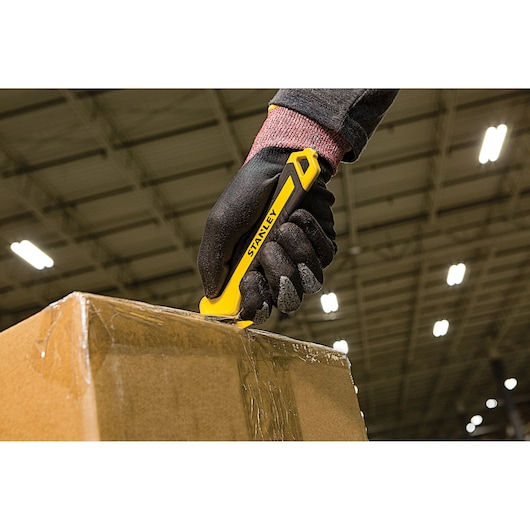 STANLEY STHT10356-0 utility knife cutting tape on a cardboard box in a warehouse setting.