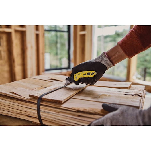 Photo of STANLEY STHT10424-0 folding utility knife cutting wood strap in construction setting.
