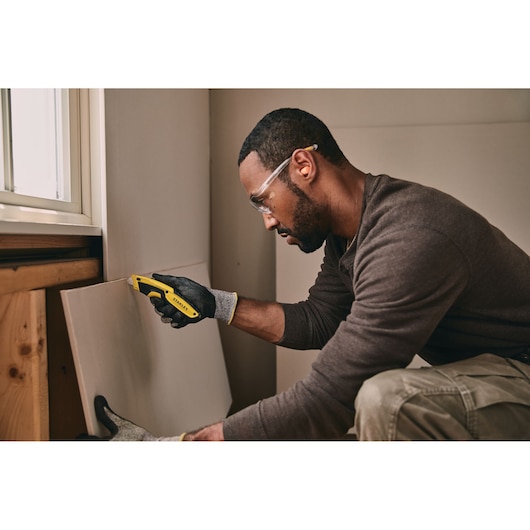 STANLEY STHT10479-0 utility knife used for drywall cutting, shown in a construction setting.