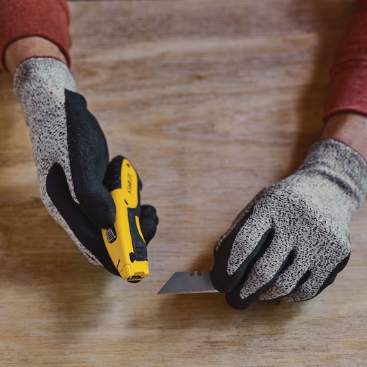 STANLEY STHT10479-0 utility knife and blade held by gloved hands on wooden surface.